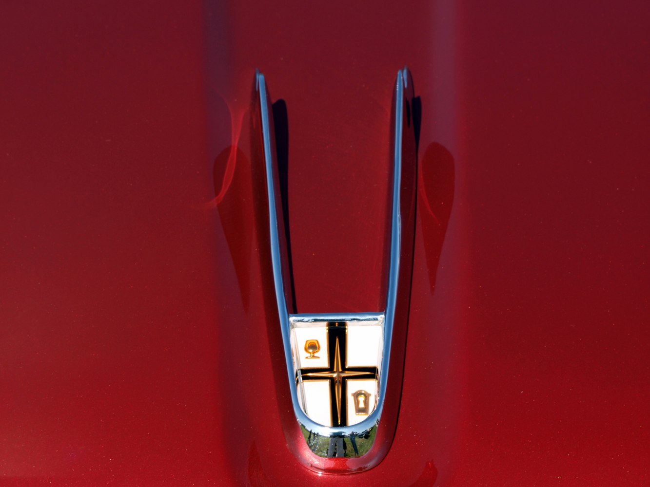 Chrome V-shaped hood ornament with emblem on red vehicle hood