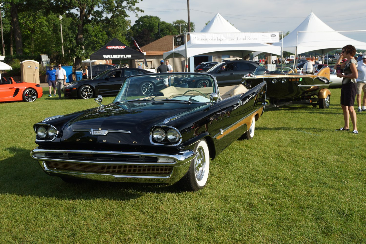 Black convertible with dual round headlights and whitewall tires on grass.