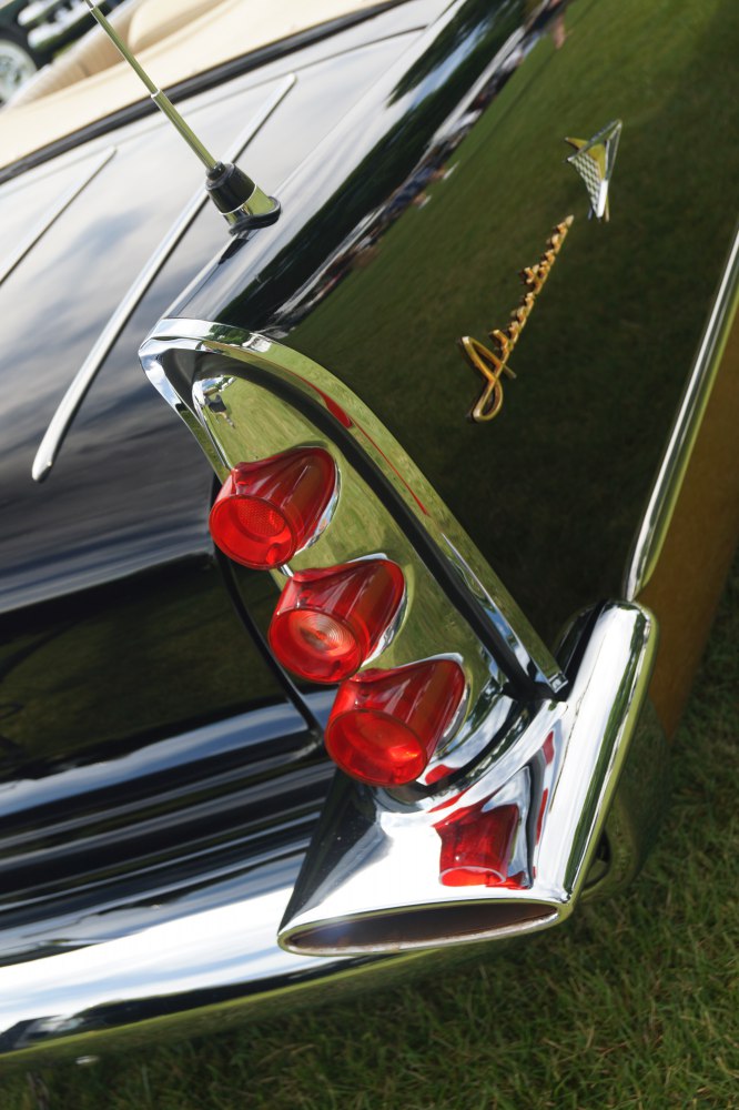 Triple red tail lights and prominent tailfin with chrome bumper and emblem on vintage convertible
