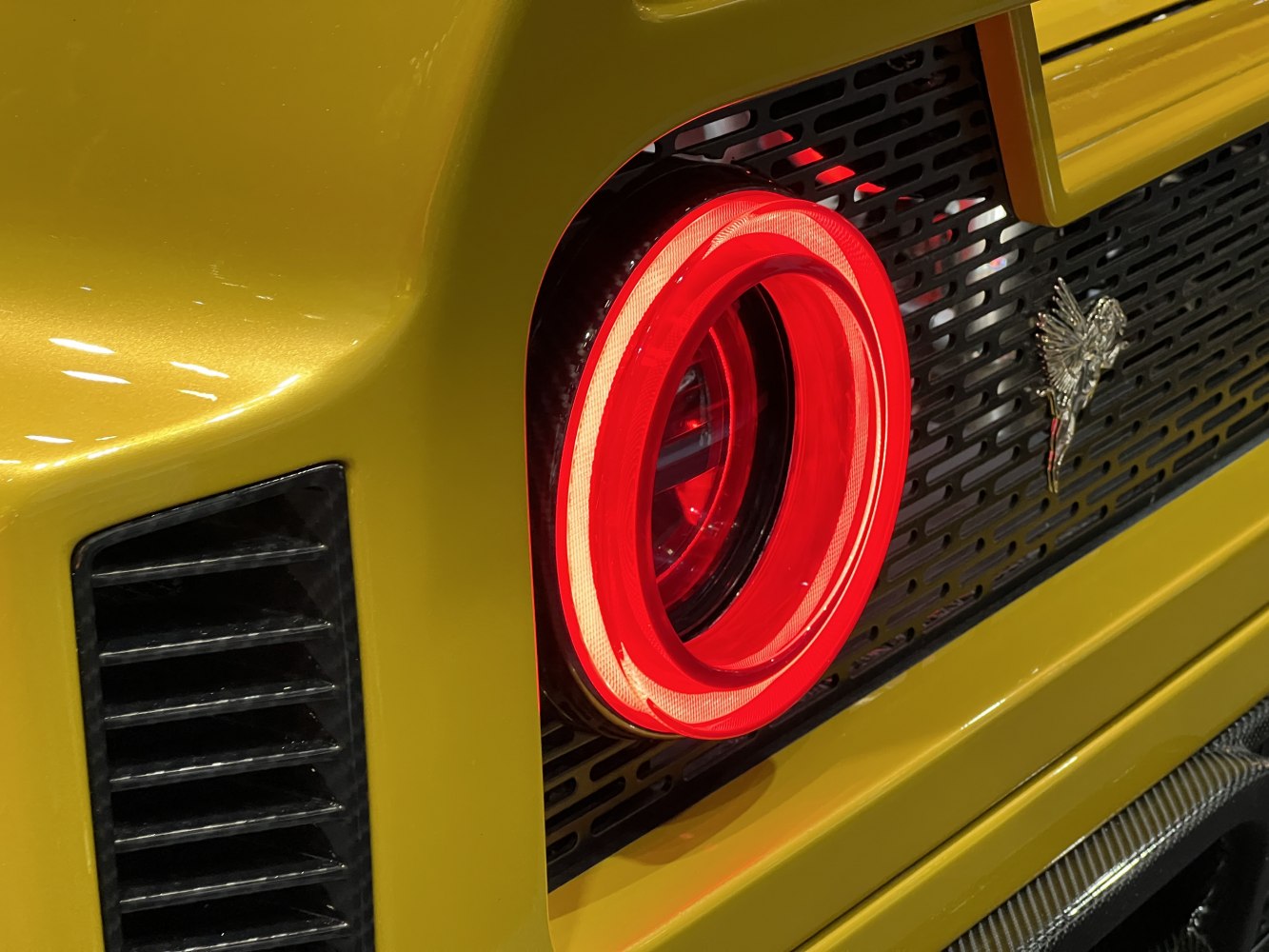 Rear circular LED taillight and ventilation grille on a yellow car body