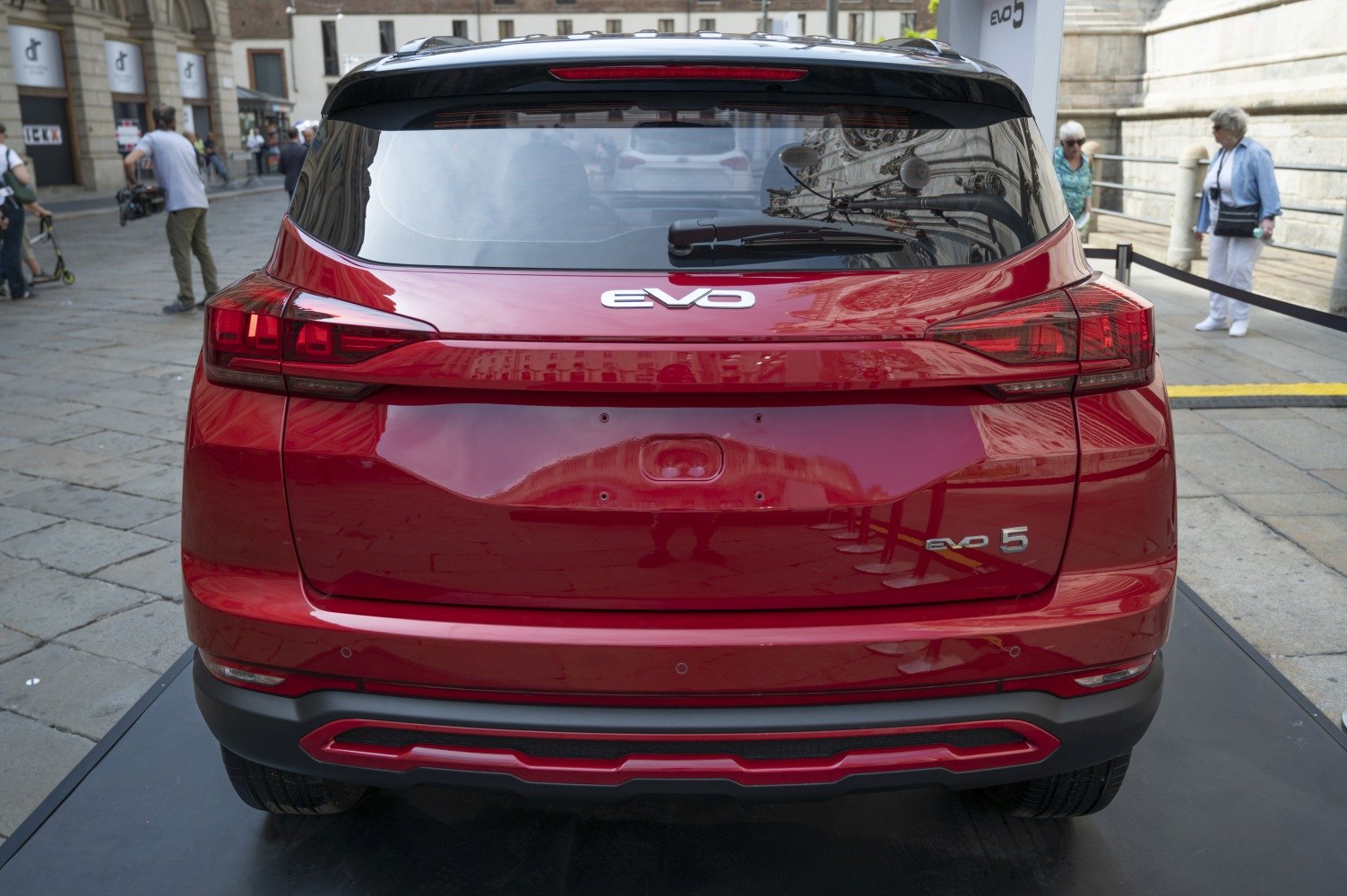 Rear view of modern red SUV with sleek taillights and black roof spoiler.
