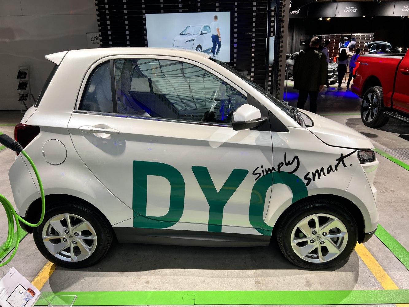 Compact electric microcar side view with charging cable connected.