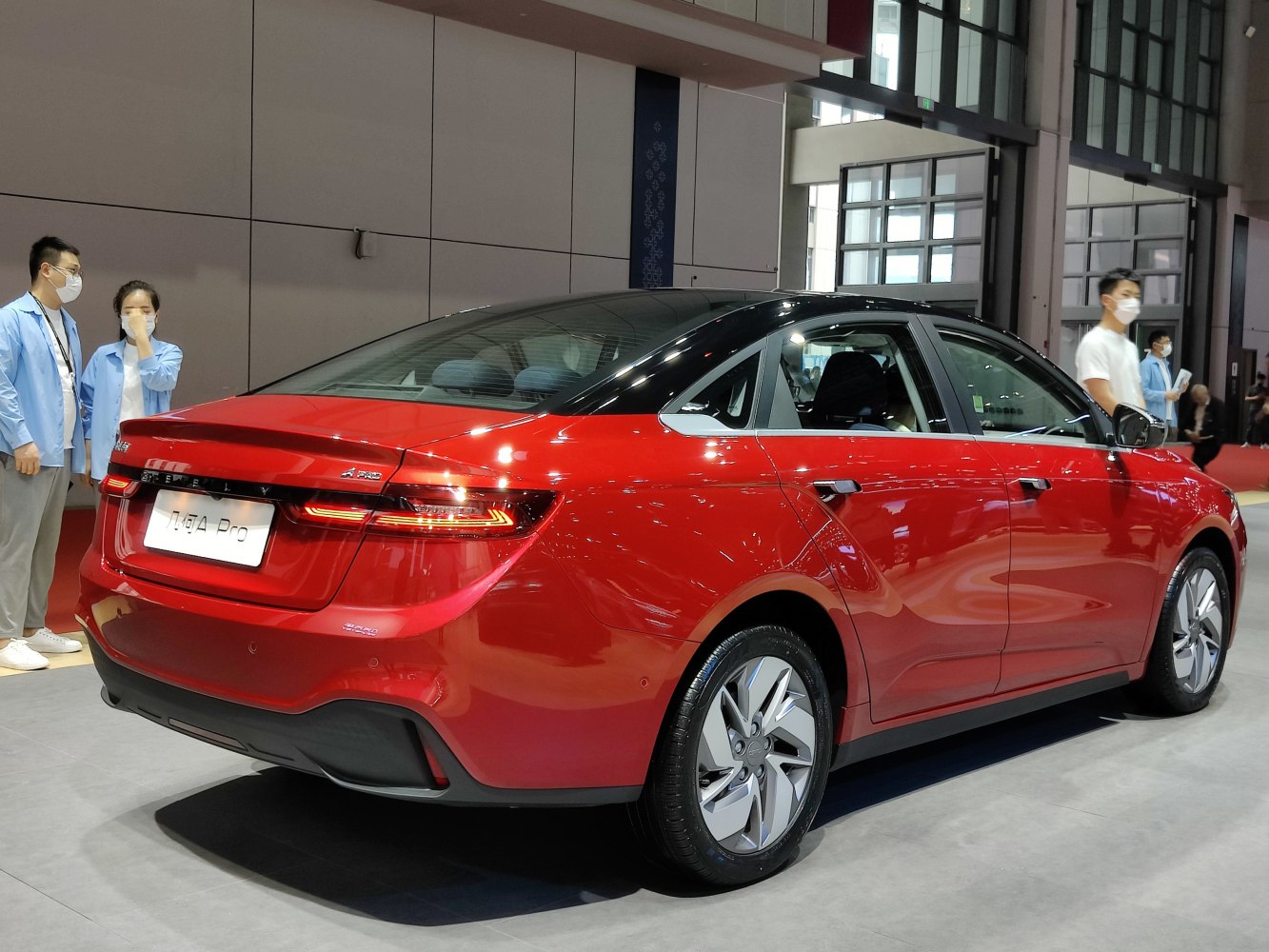 Red sedan rear three-quarter view with sloping roofline and illuminated tail lights