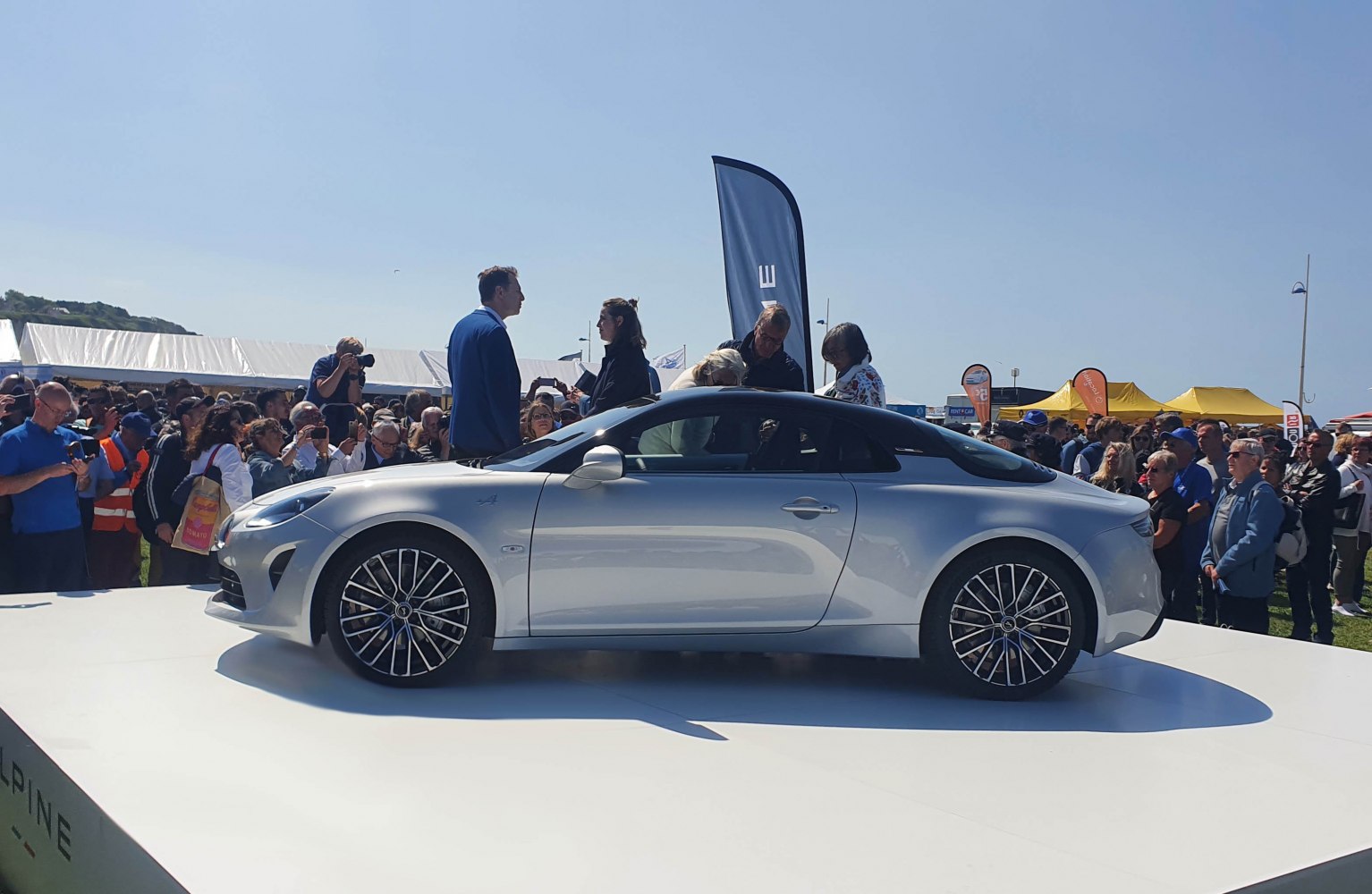 Side profile of a silver sports coupe car with alloy wheels on a platform.