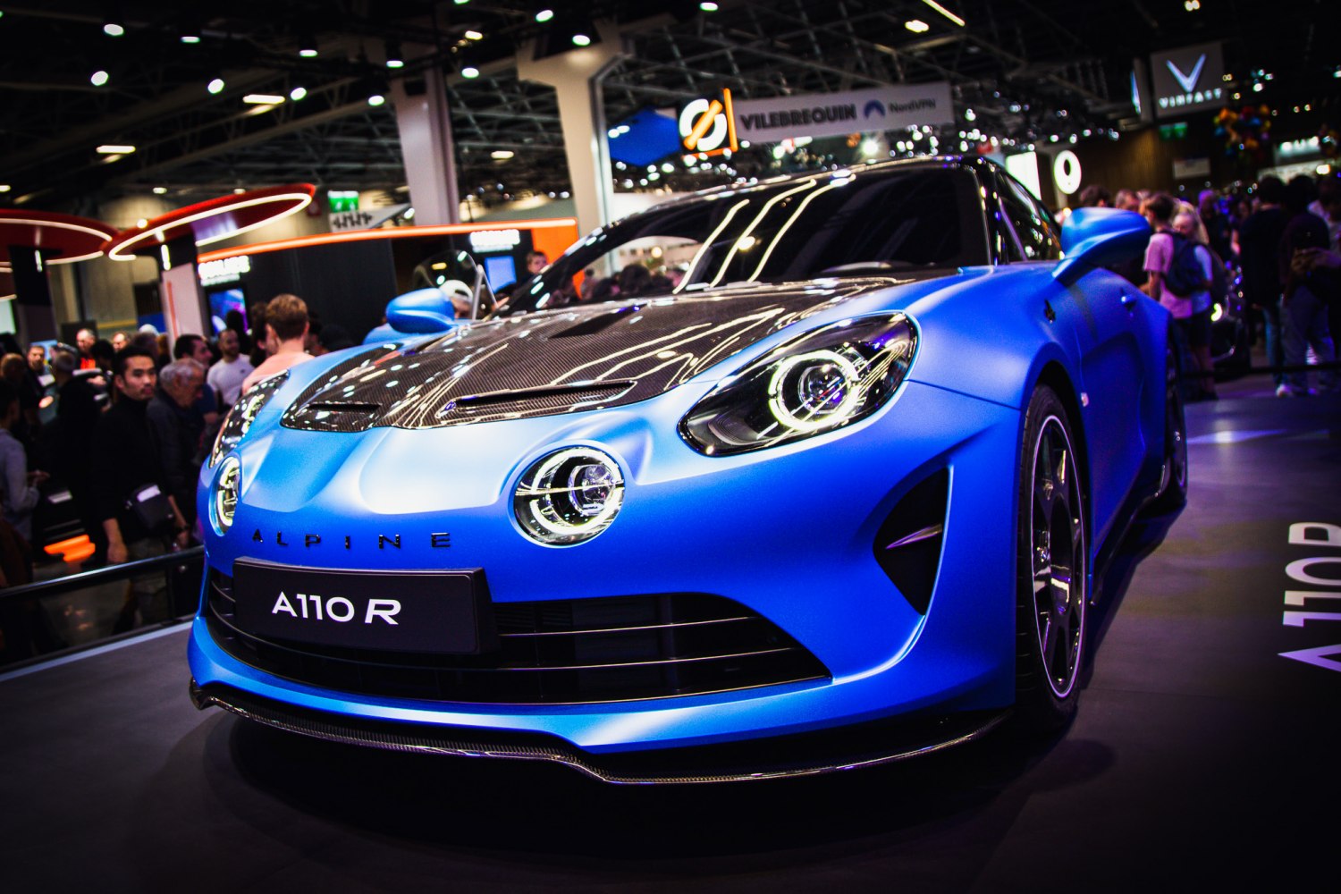 Front view of matte blue sportscar with circular LED headlights and carbon fiber hood