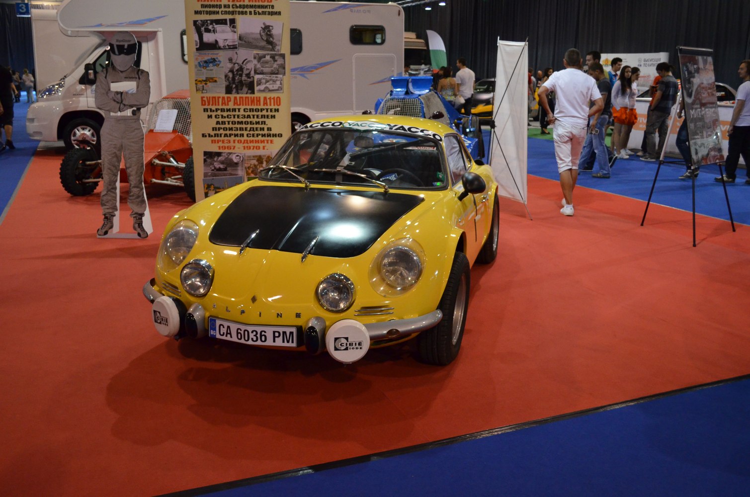 Yellow vintage rally car with black hood and four front spotlights.