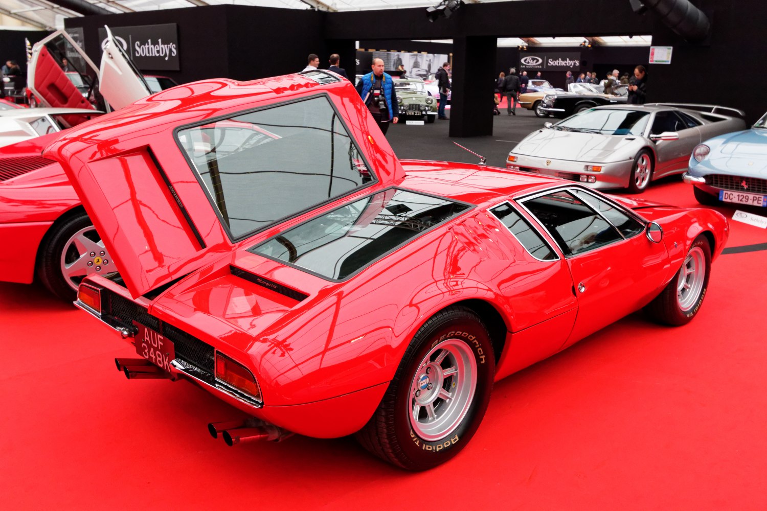 Red mid-engine sports coupe with open rear hatch and rear glass panel