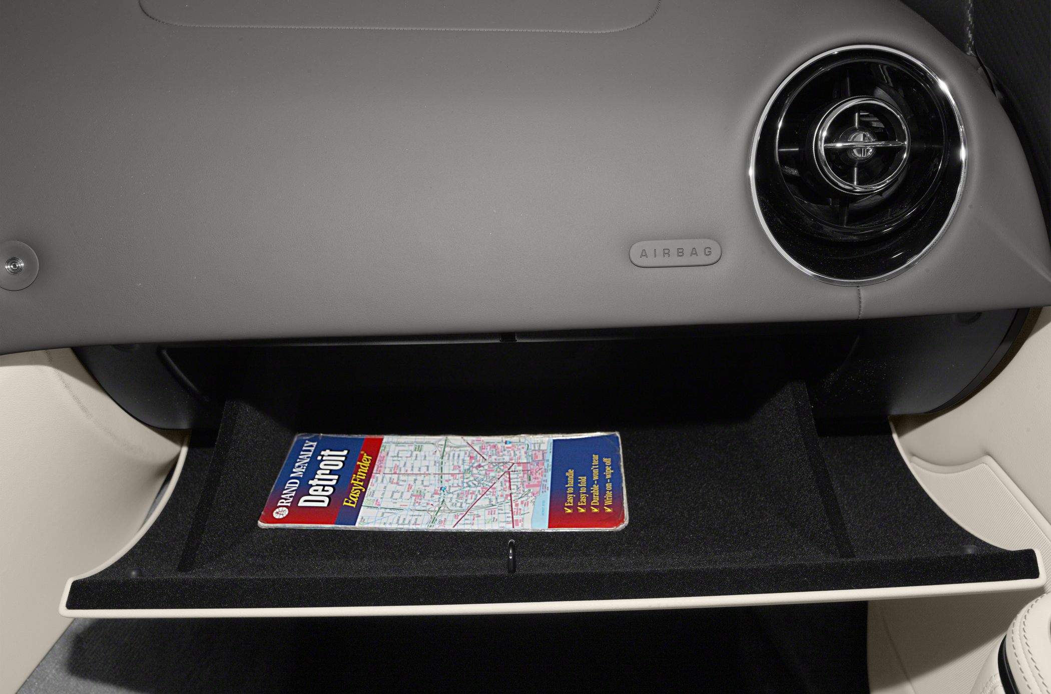 Open glove compartment with a Detroit map inside and nearby air vent.