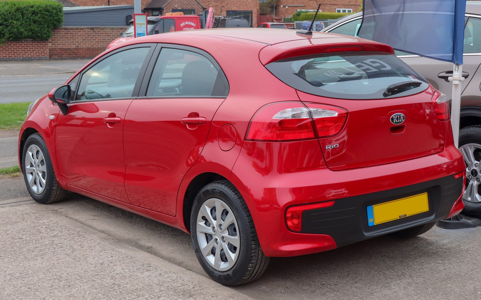 Red five-door hatchback showing rear side, clear taillights, alloy wheels