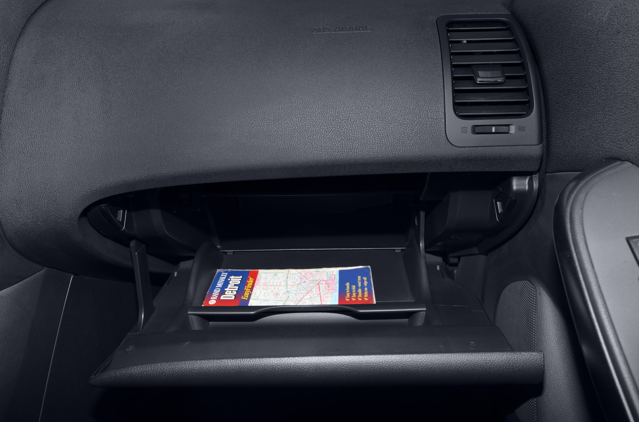 Open glove box with a map inside and adjacent dashboard air vent
