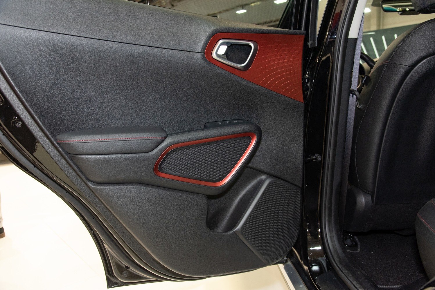 Rear door interior with speaker, red accent trim, and window controls