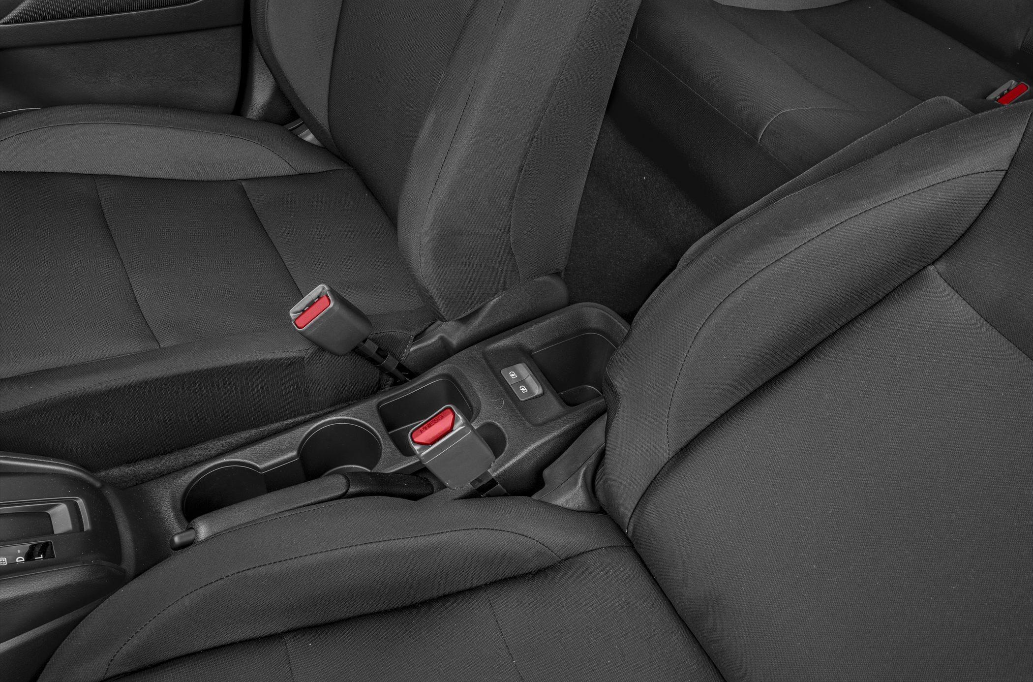 Close-up of car seats, seatbelt buckles, center console with cup holders and control buttons.