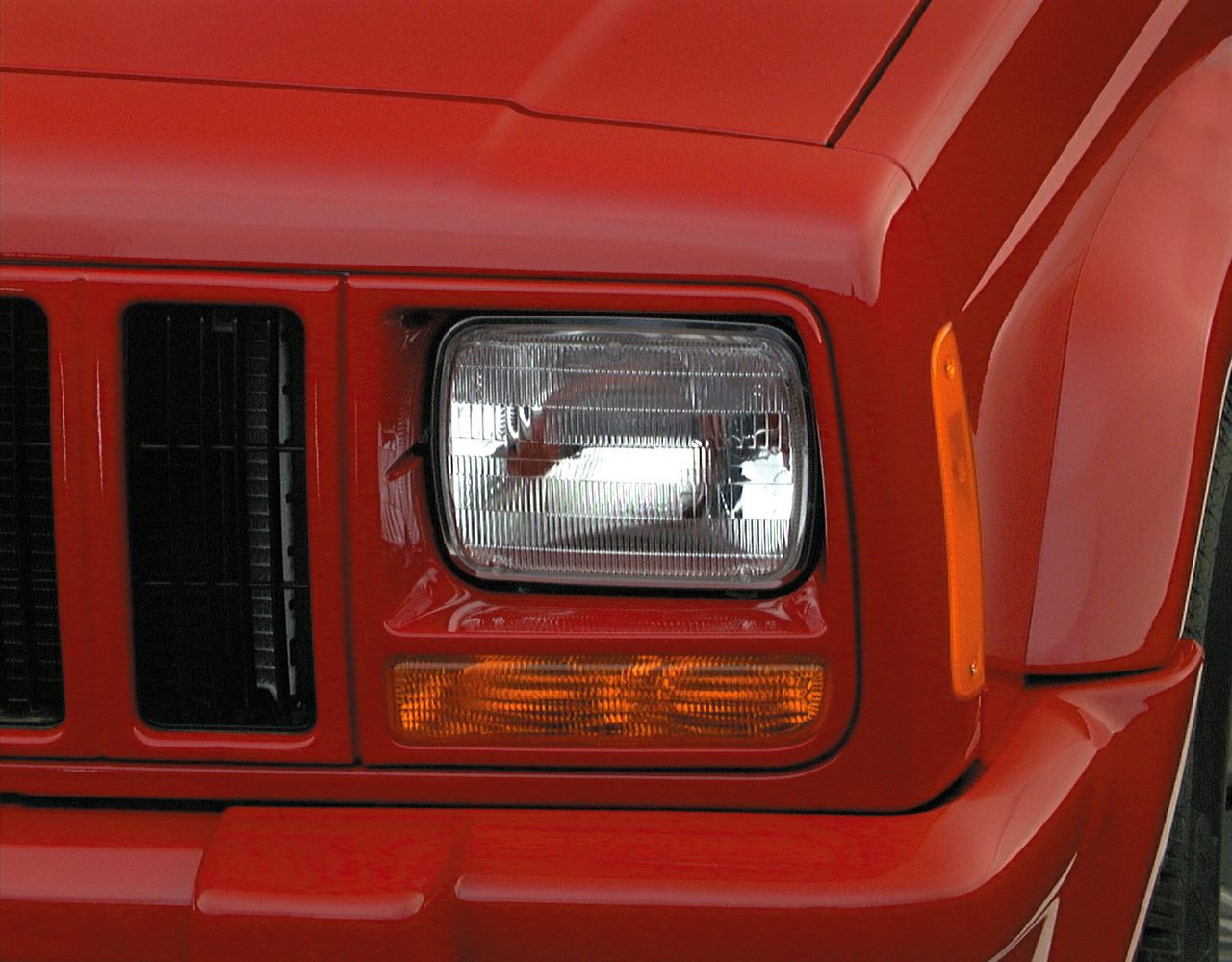 Rectangular front headlight and amber indicator of red SUV.