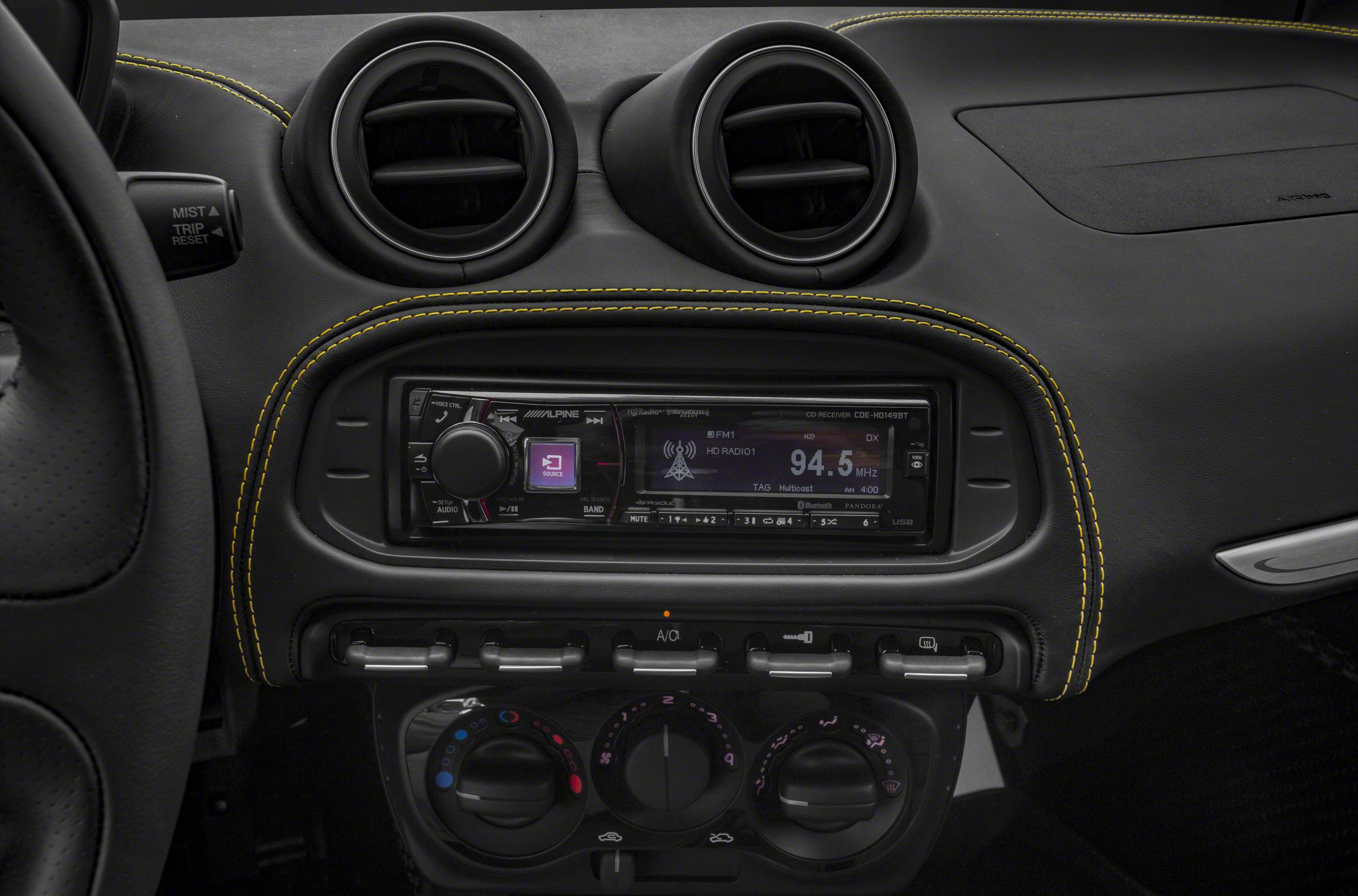 Dashboard with dual air vents, Alpine radio, and climate control knobs with yellow stitching