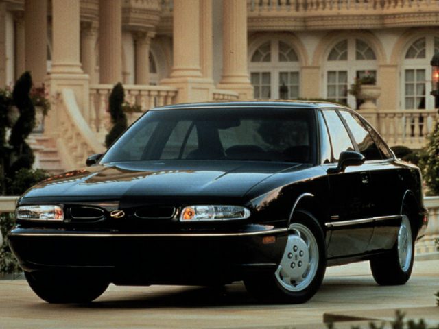 Front angled view showcasing dual headlights and rounded sedan body.