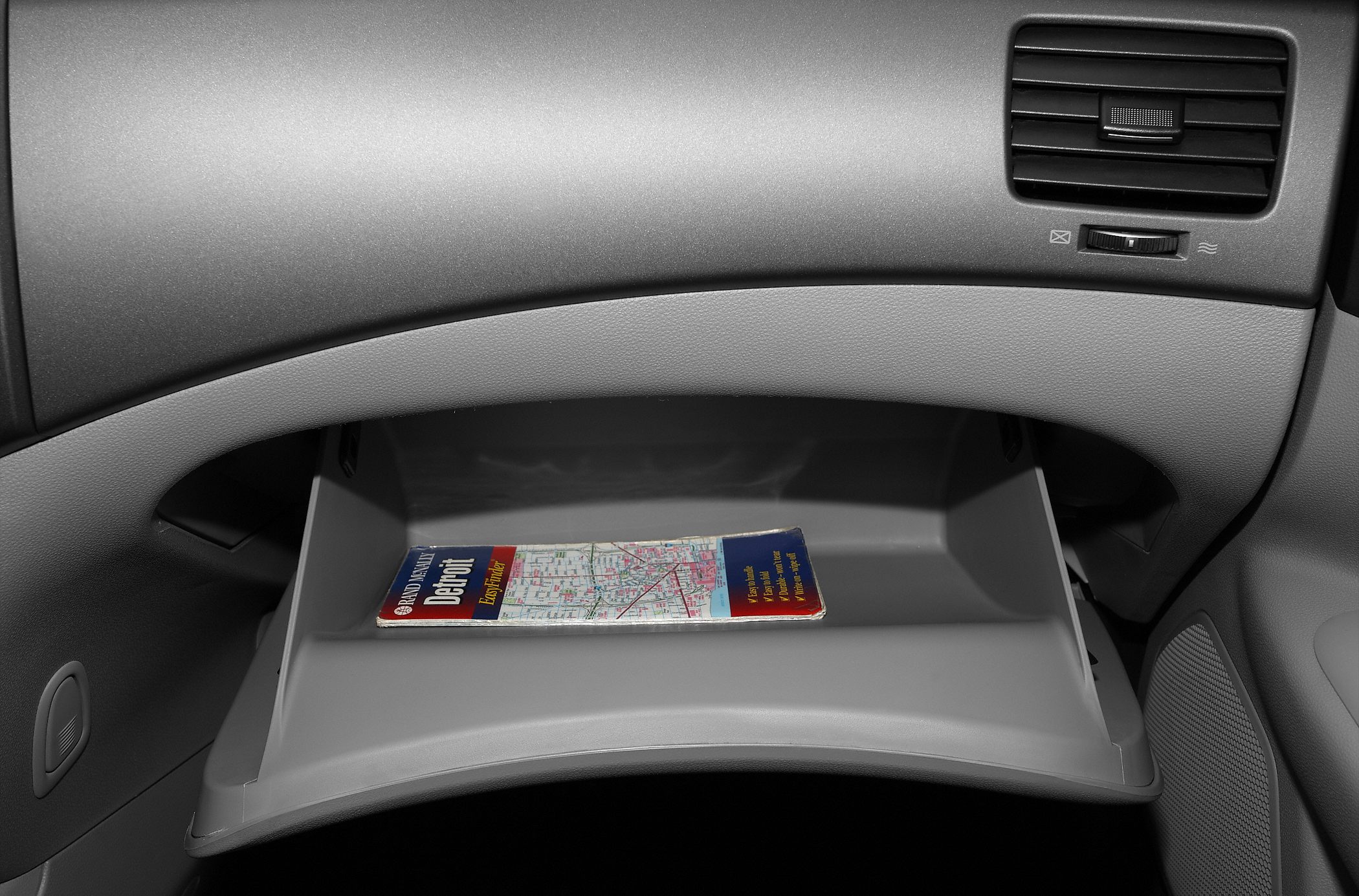 Open glove box with map and nearby air vent inside car dashboard.