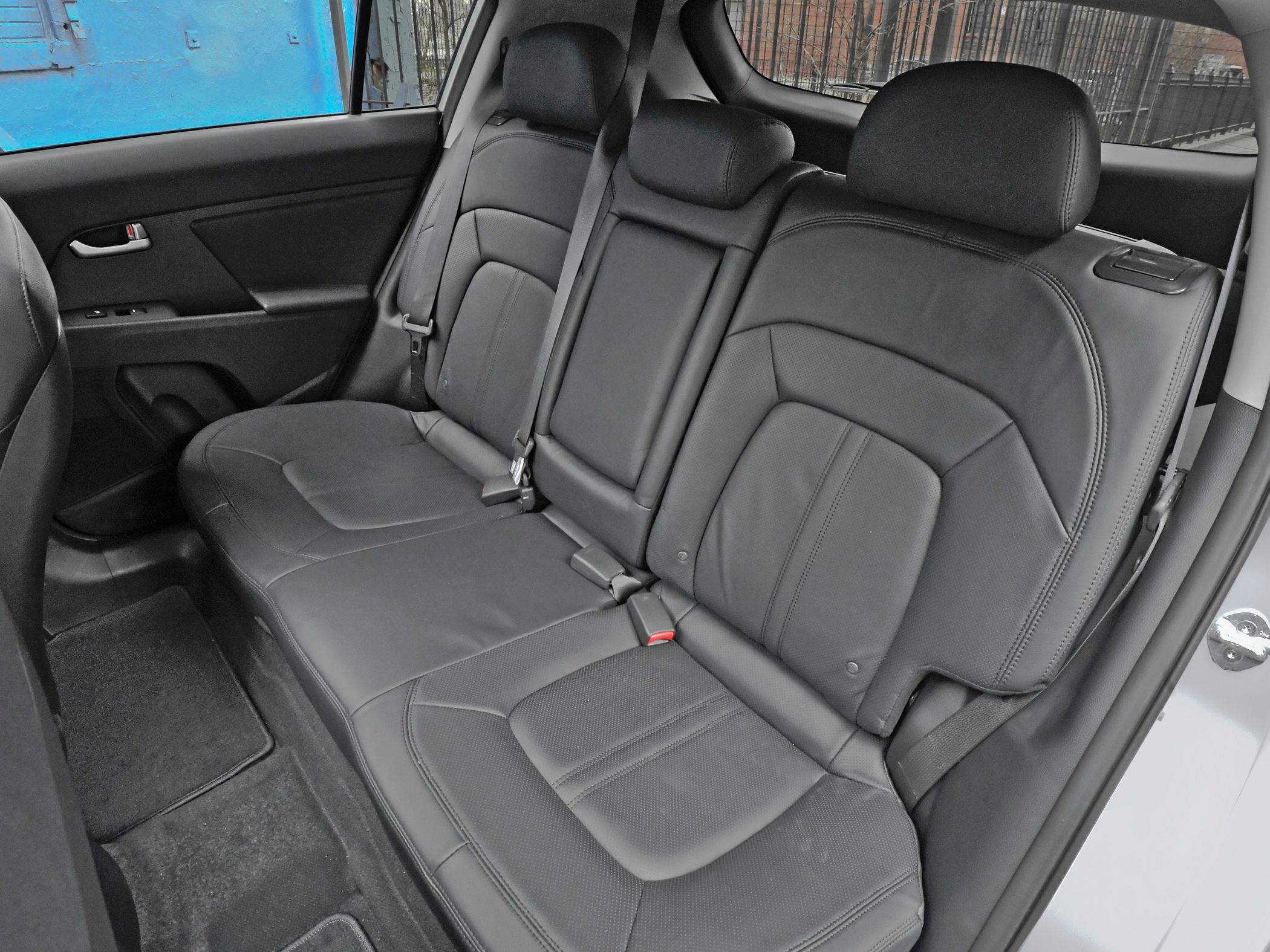 Rear black leather car seats with three headrests and seat belts.