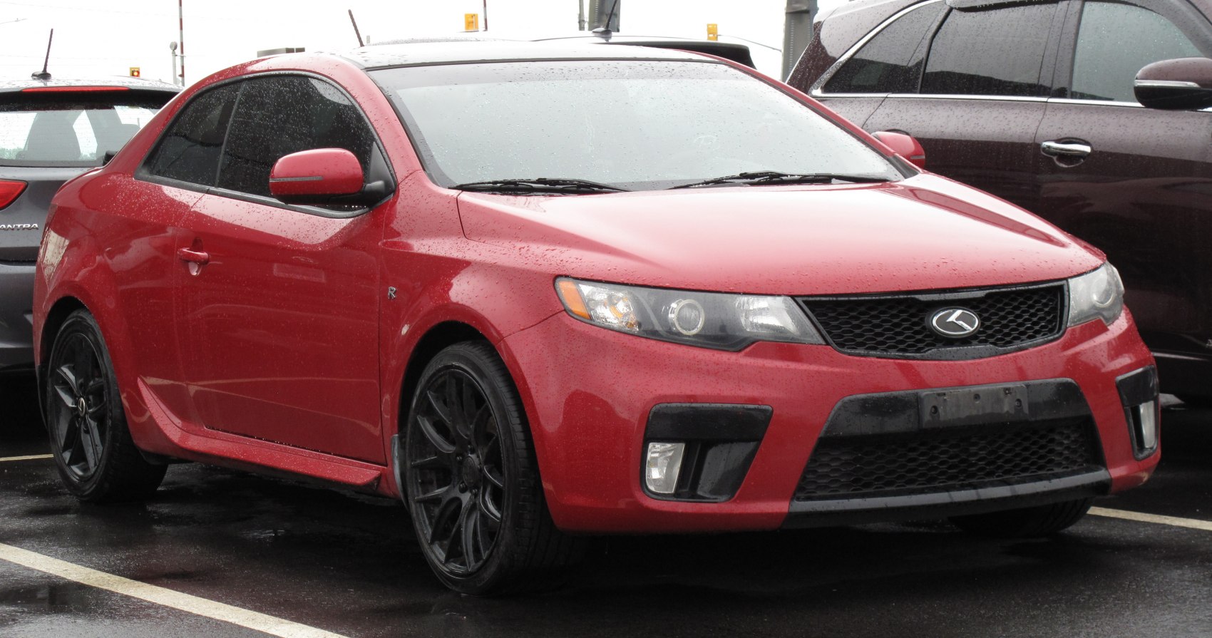 Red sport compact coupe with black alloy wheels and aggressive front grille