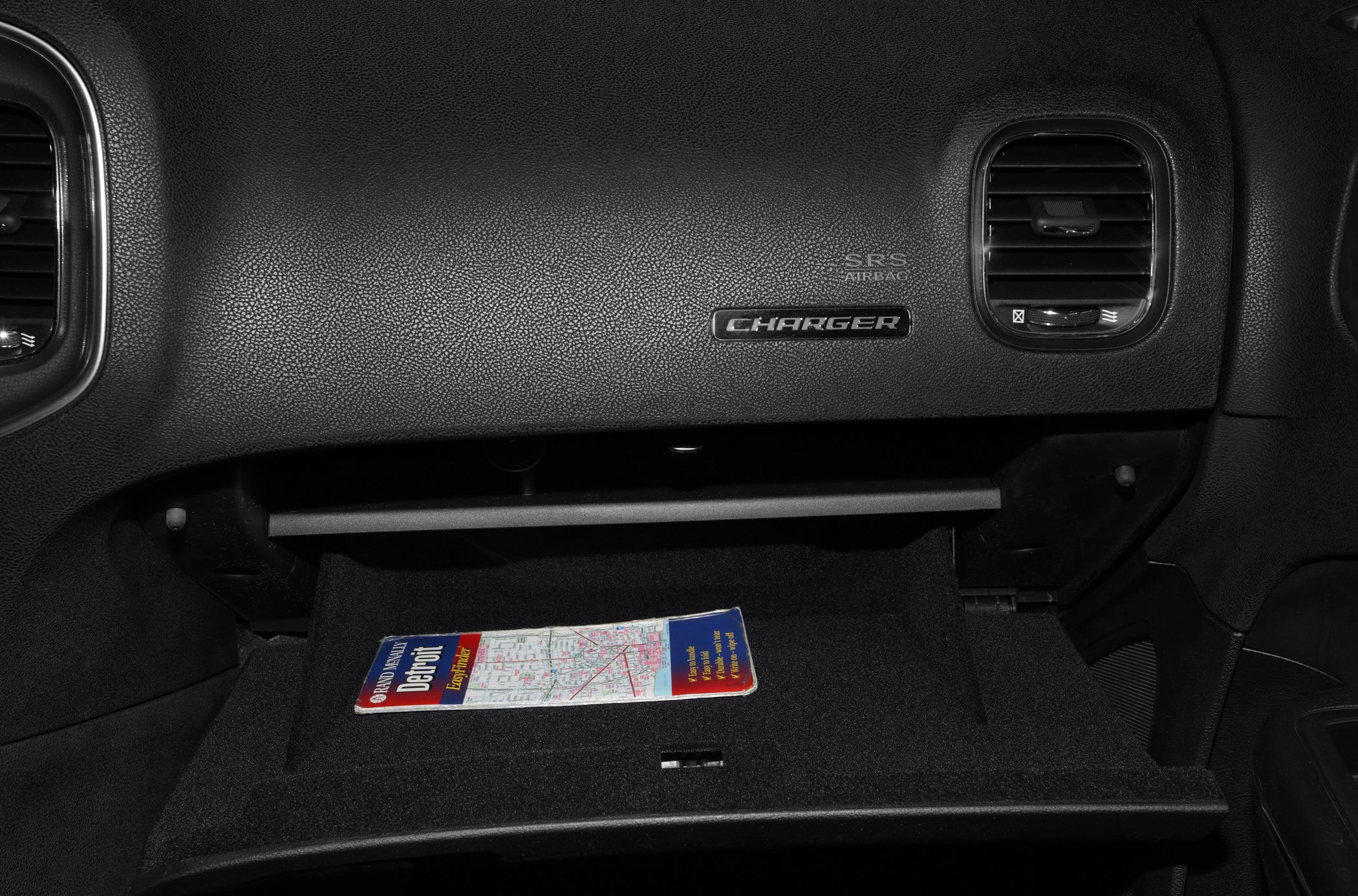 Dashboard glovebox open with Charger emblem and air vents