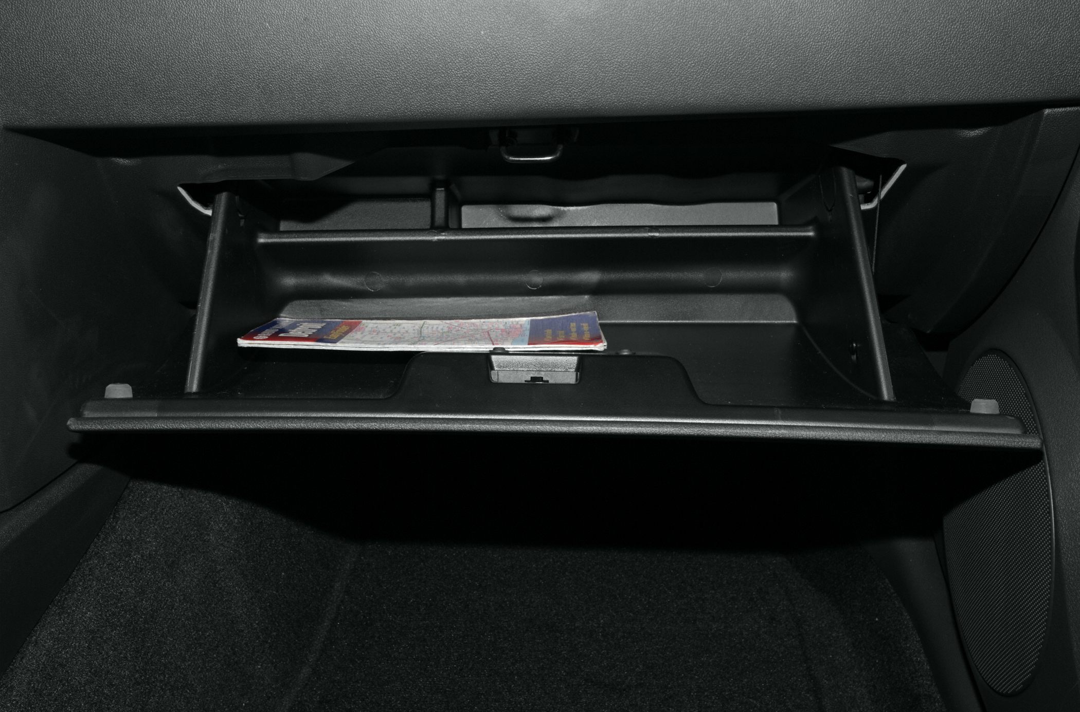 Open glove box compartment with a map inside and speaker next to it