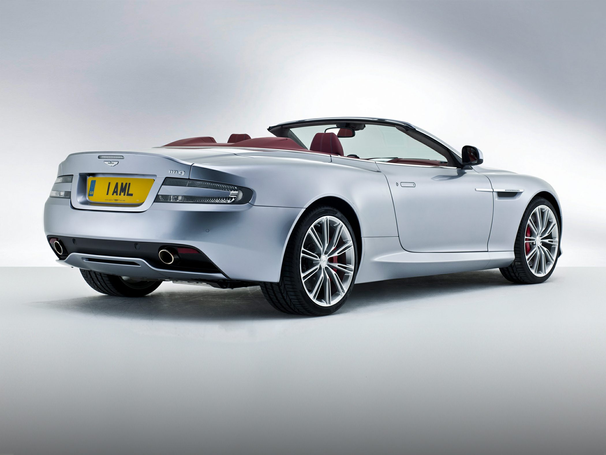 Silver convertible with dual exhaust and red interior, rear-side angle