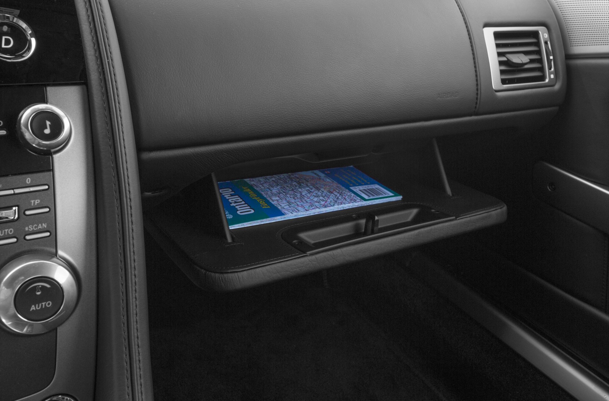 Glove compartment with a visible map inside, leather dashboard and air vent in luxury coupe interior.