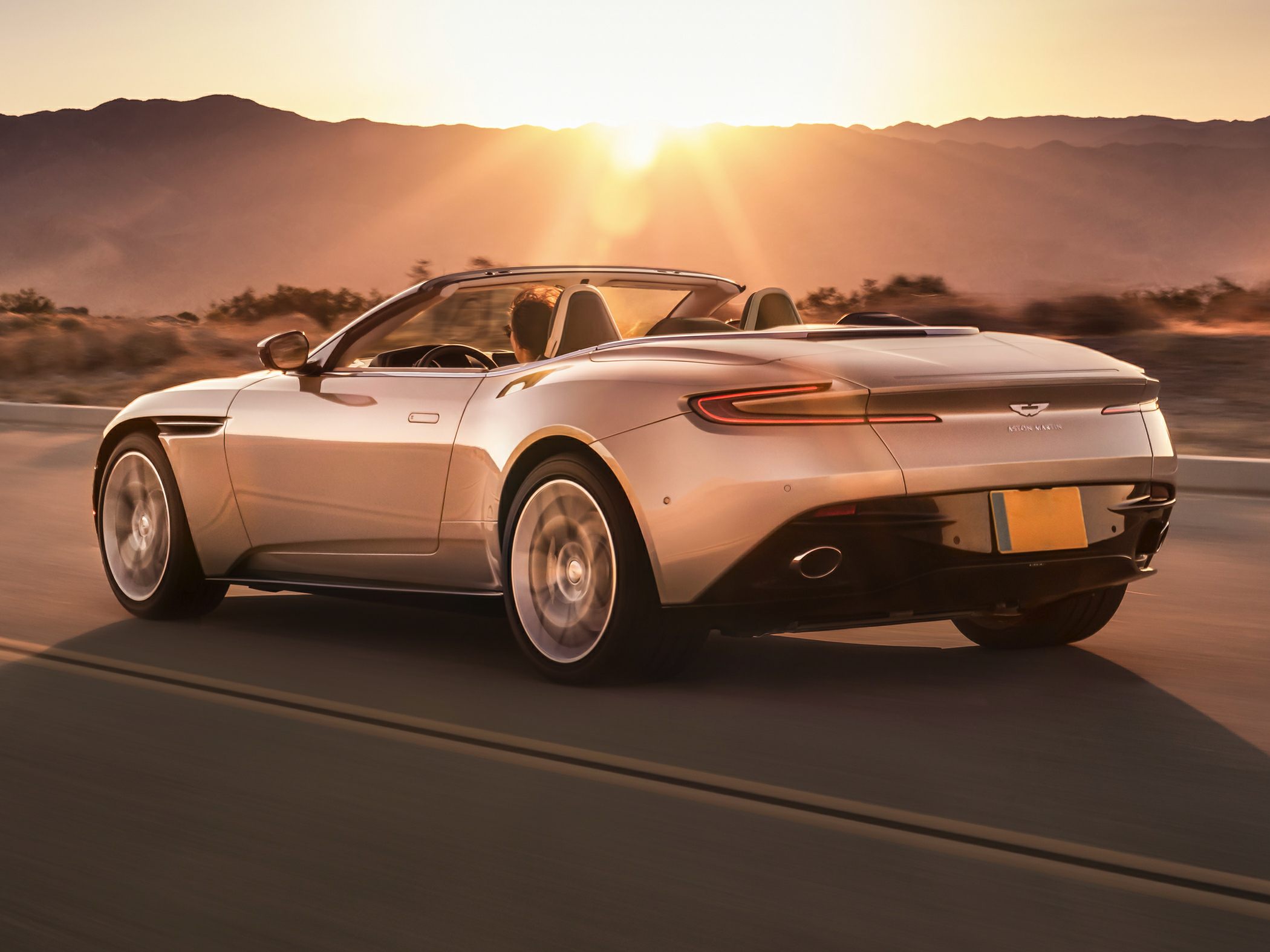 Rear view of sleek luxury convertible with open roof driving at sunset.