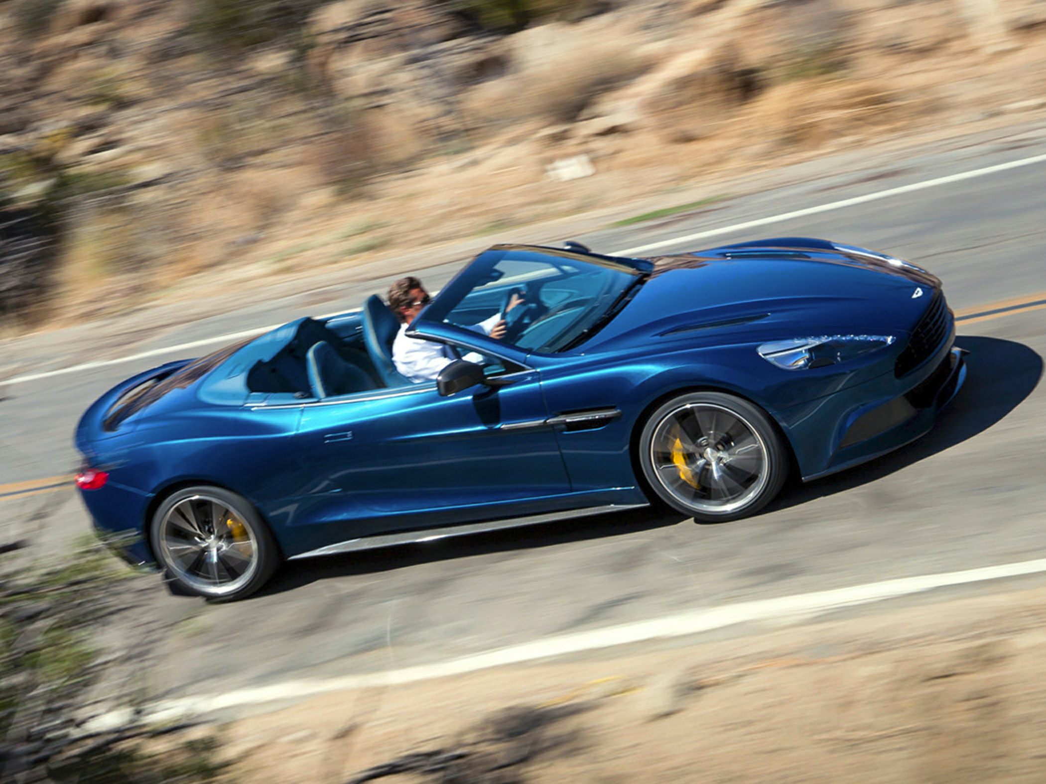 Blue convertible sports car driving dynamically on a winding road
