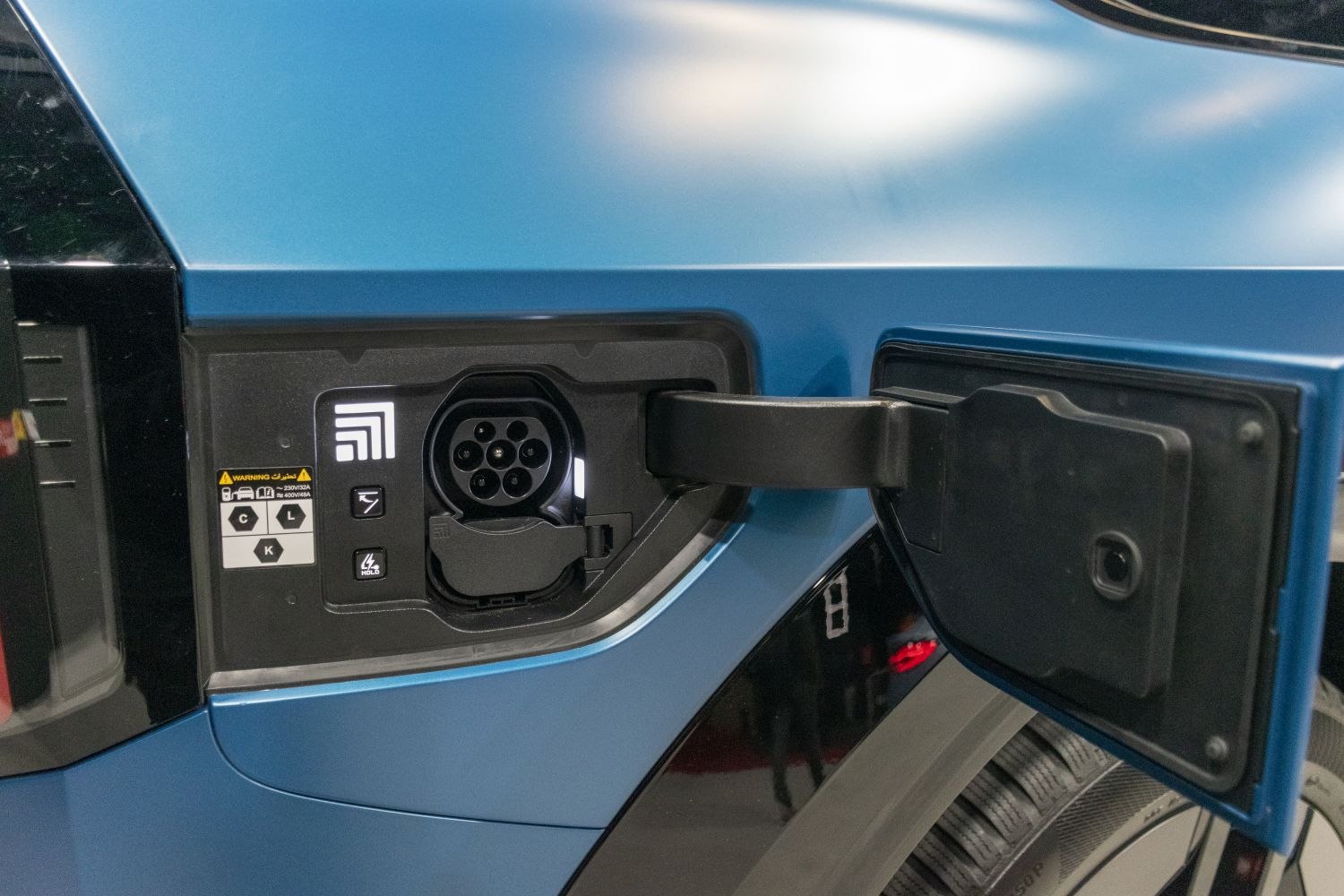 Close-up of electric vehicle charging port with connector on blue body panel