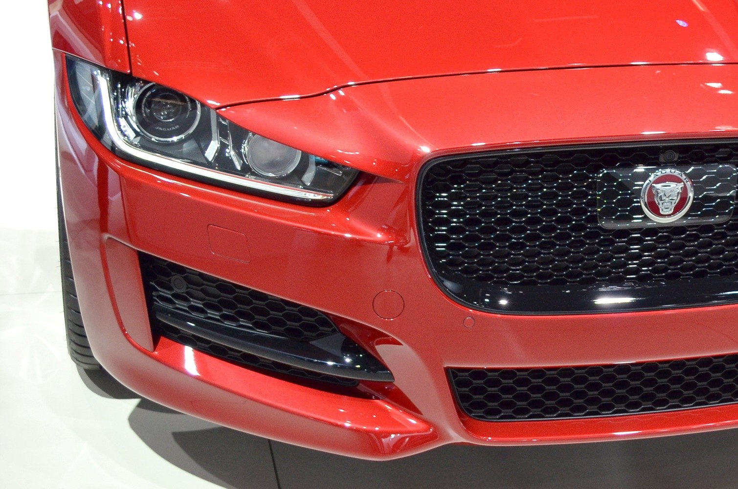 Close-up of front headlight and black honeycomb grille on red car