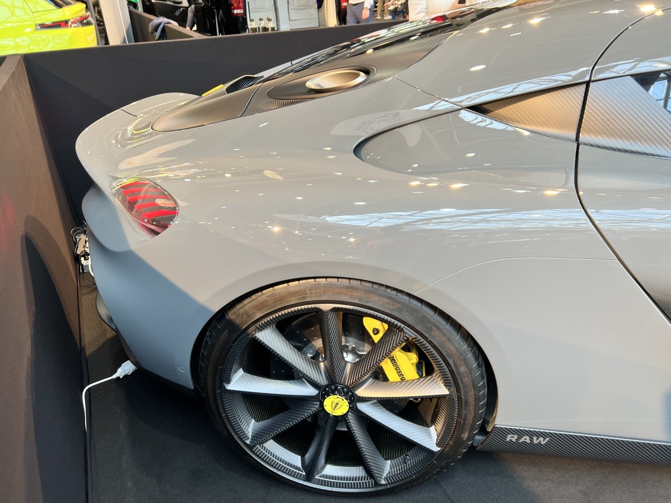 Rear wheel with carbon fiber rim and yellow brake caliper on sleek gray sports vehicle