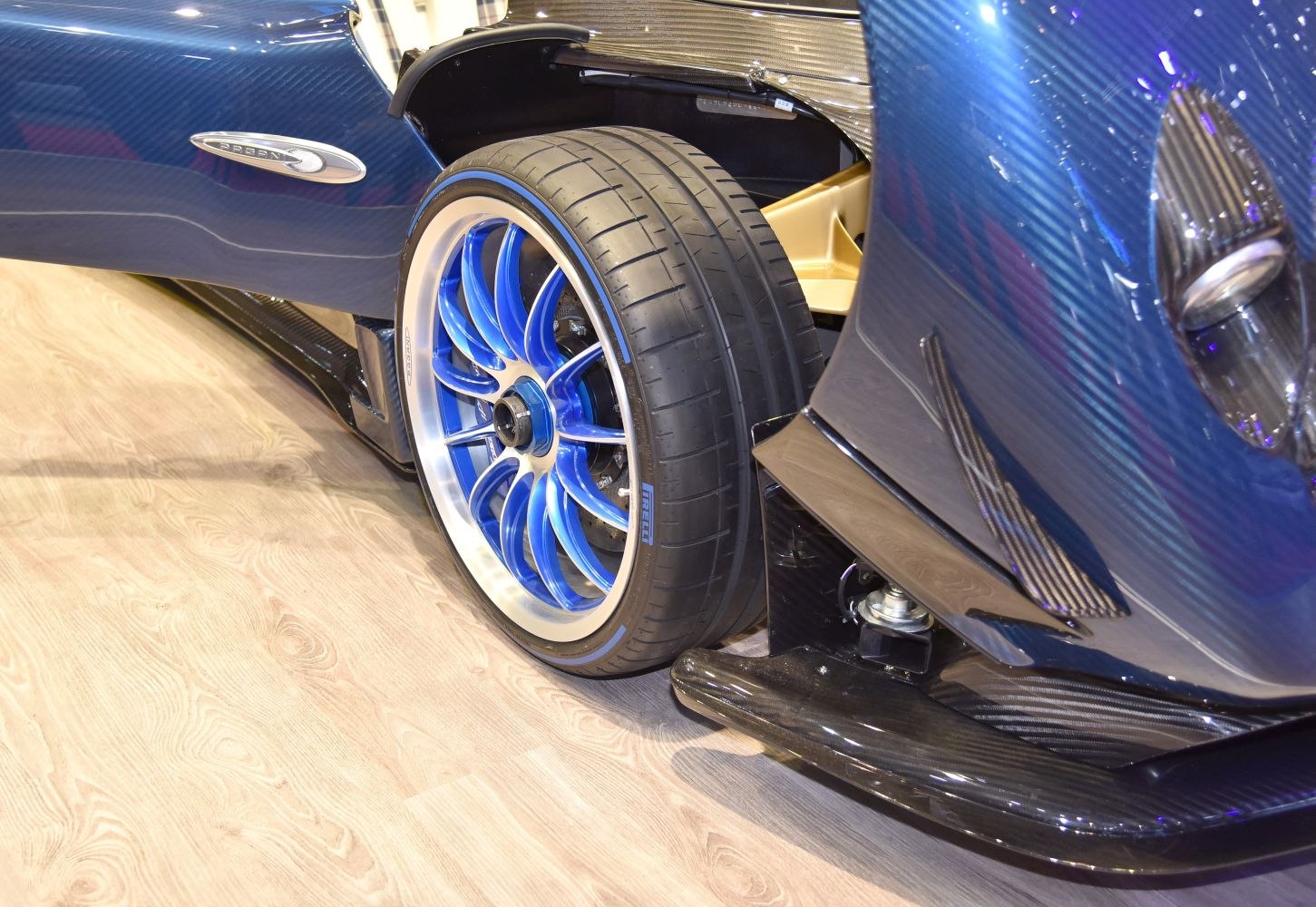Blue aluminum alloy wheel with Pirelli tire and carbon fiber body panel.