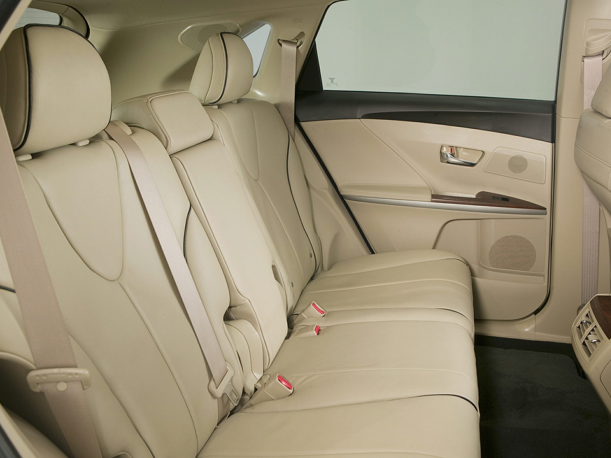 Beige leather rear seats with seat belts and door panel with wooden trim.