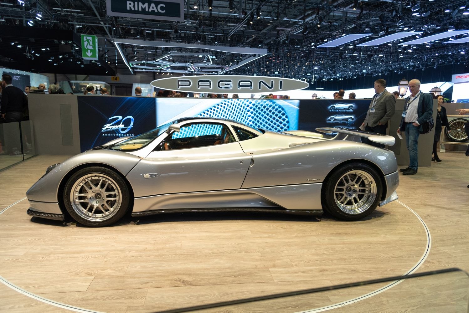 Sleek silver sports car side profile with prominent rear wing and multi-spoke wheels.