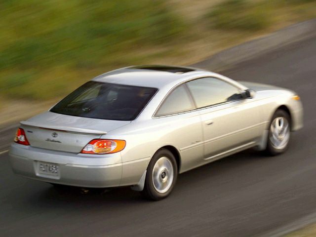 Rear and side view of a silver coupe with illuminated taillights in motion