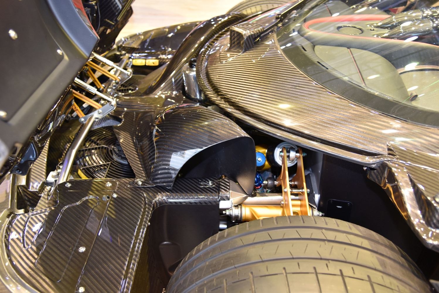 Carbon fiber rear suspension and tire close-up with gold-colored suspension arms.