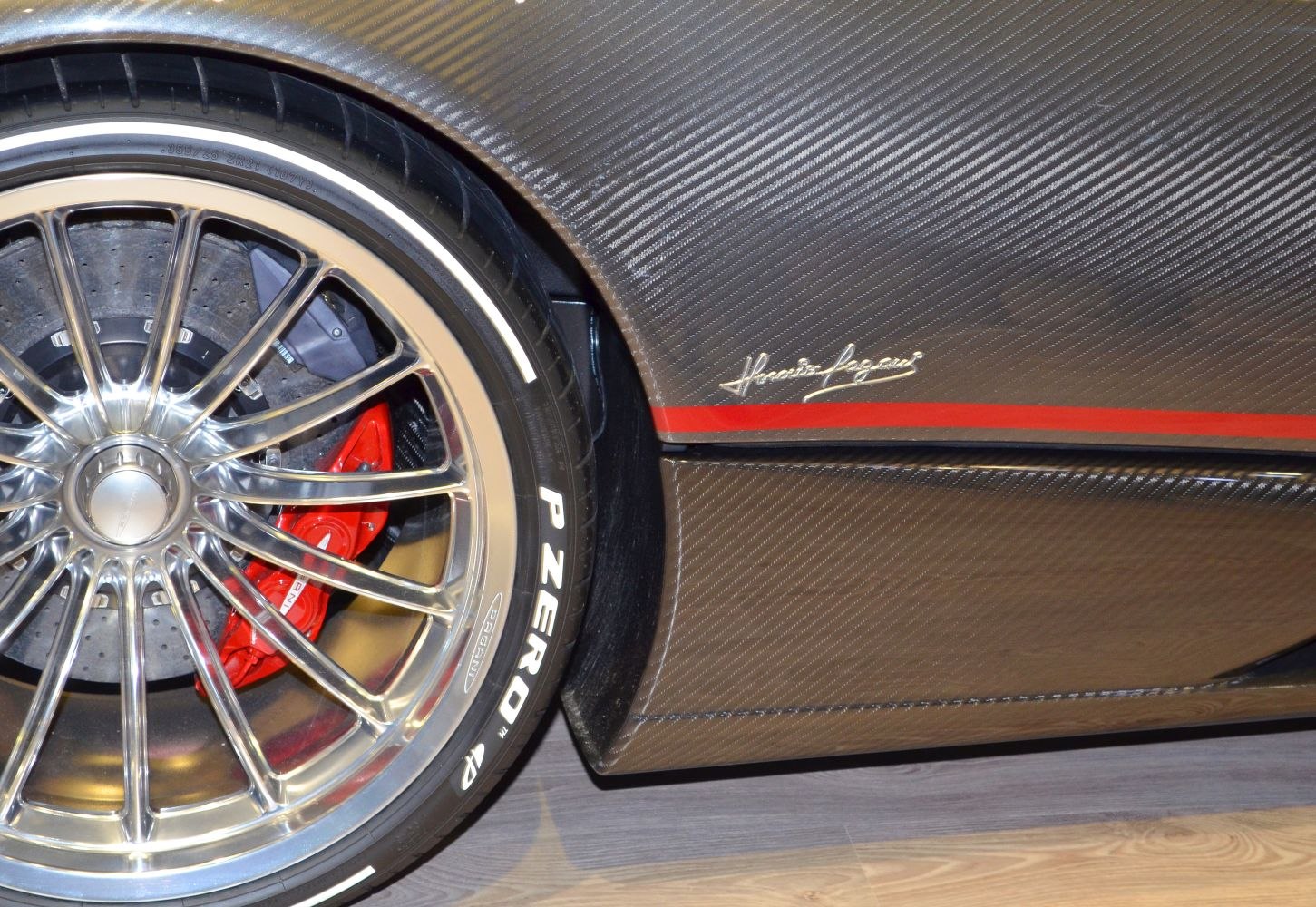 Multi-spoke polished wheel, red brake caliper, carbon fiber panel with signature and red stripe