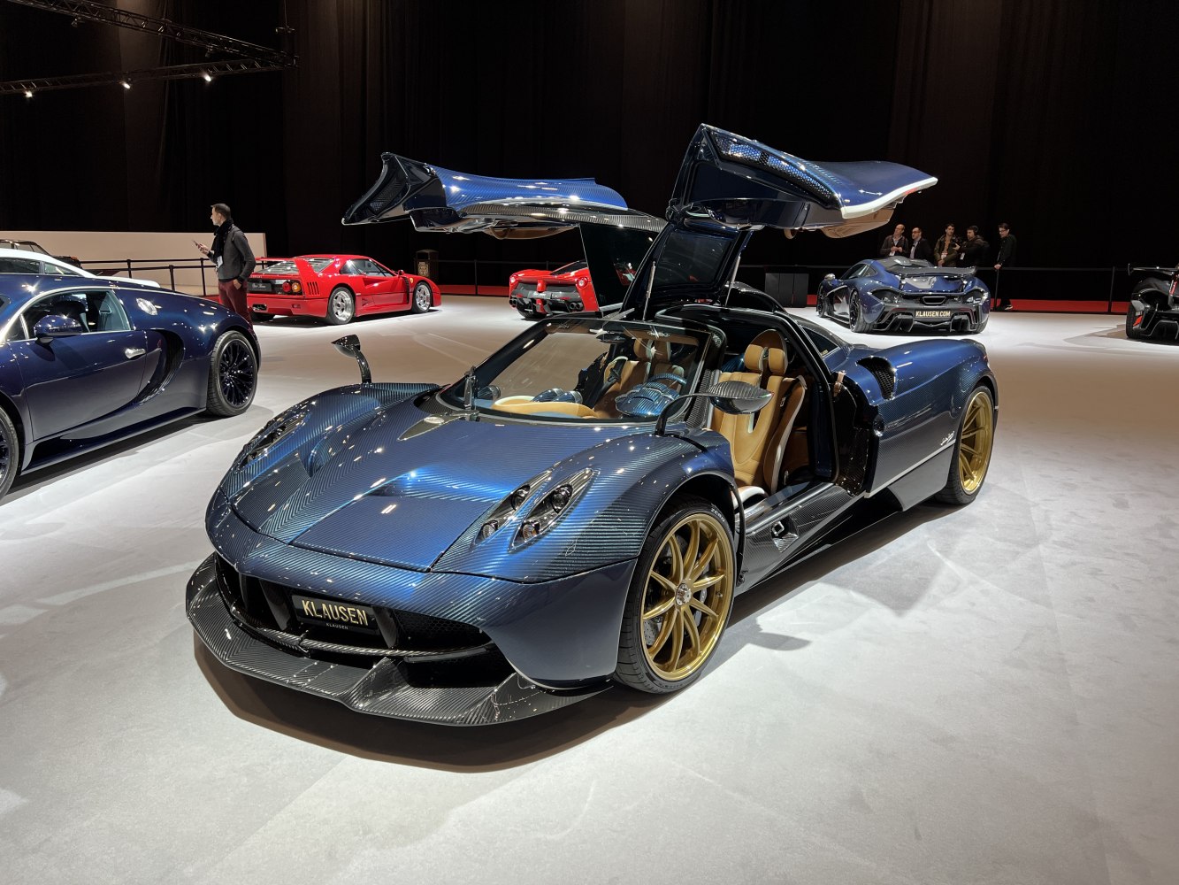 Gullwing doors and carbon fiber body of a luxury supercar with gold wheels.