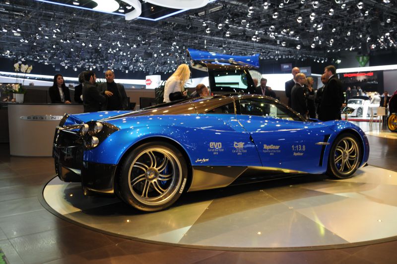 Blue supercar side profile with carbon fiber accents and gull-wing door open.