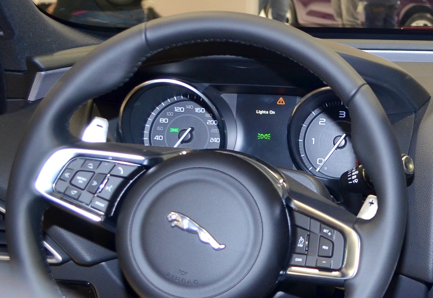 Steering wheel with multifunction buttons and instrument cluster with speedometer and tachometer.