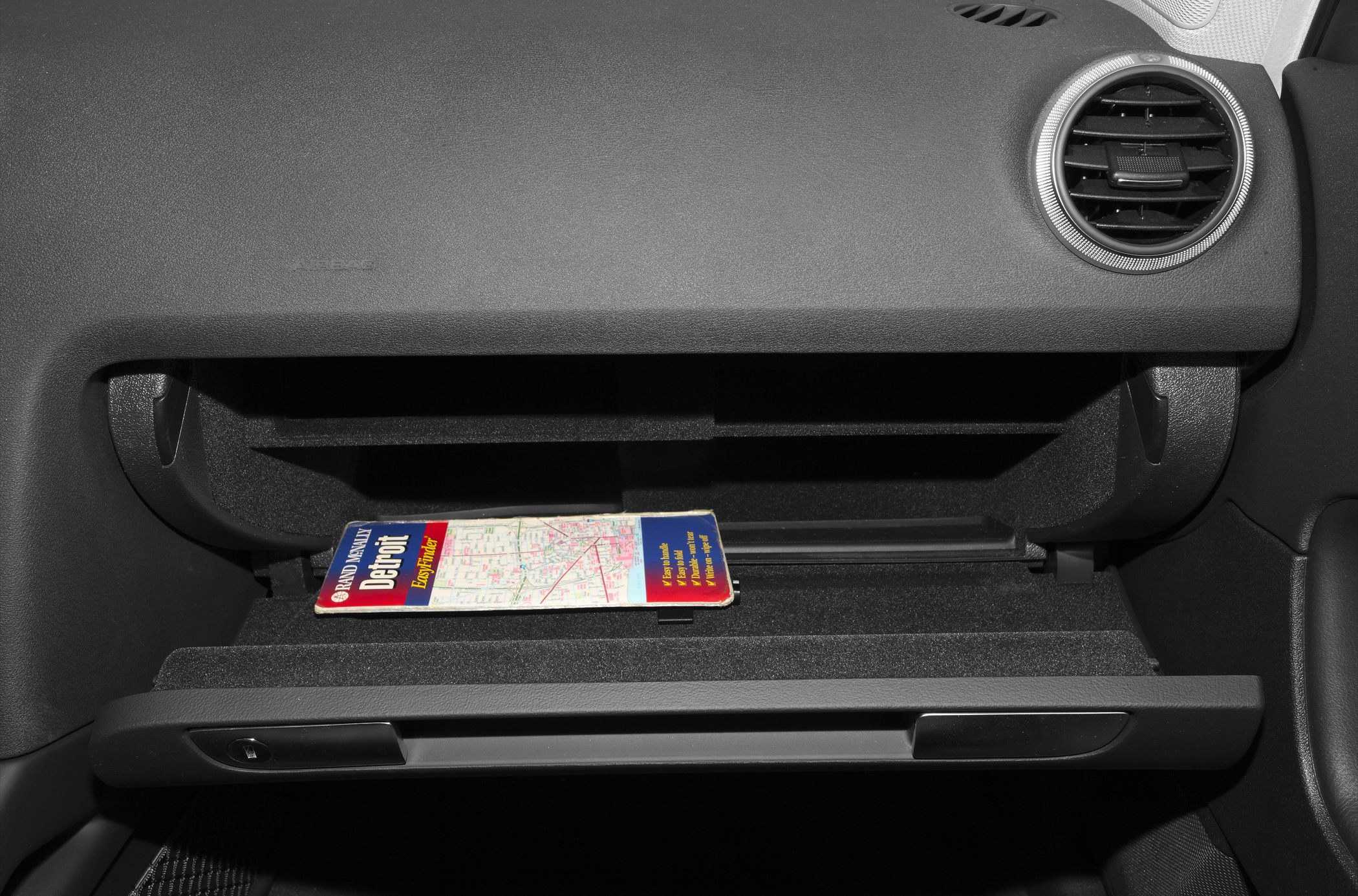 Open glove box with map and round air vent on dashboard