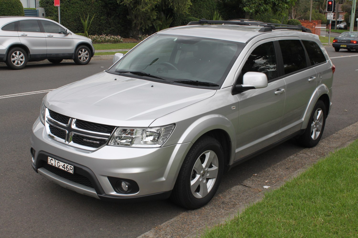 Silver SUV with chrome crosshair grille and roof rails parked by curb
