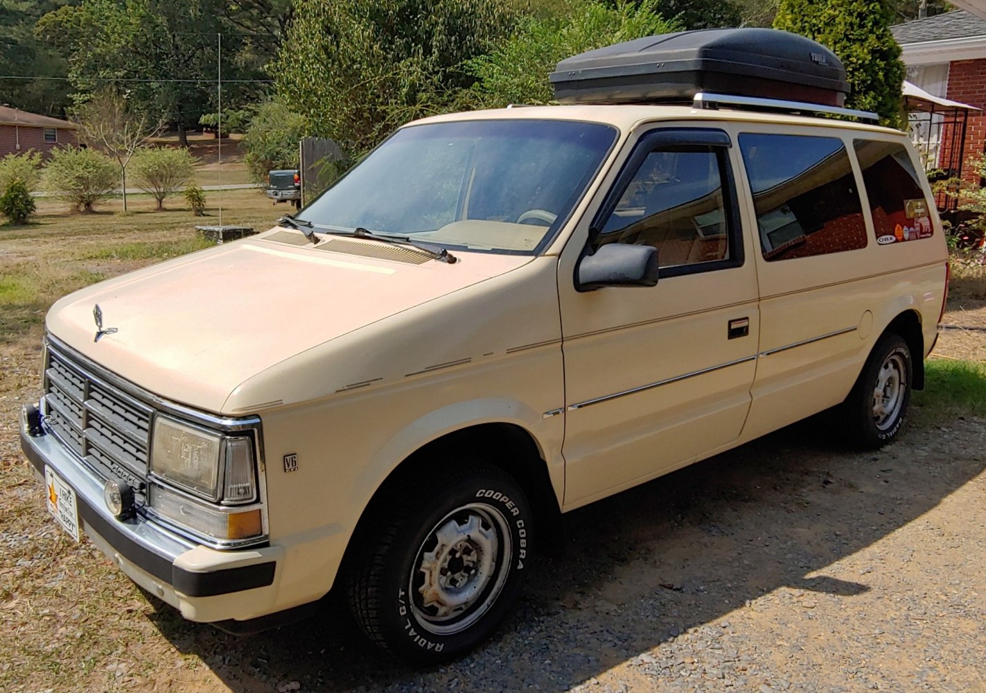 Front and side view of beige minivan with roof cargo box.