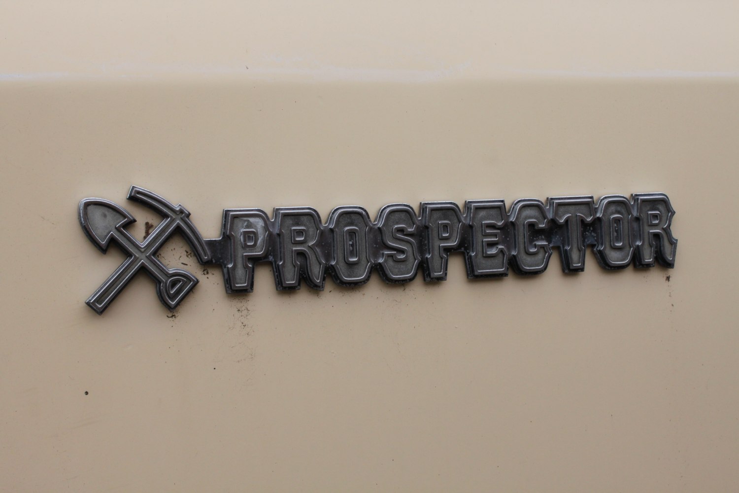 Vintage metal Prospector emblem with crossed pickaxe and shovel on vehicle body.