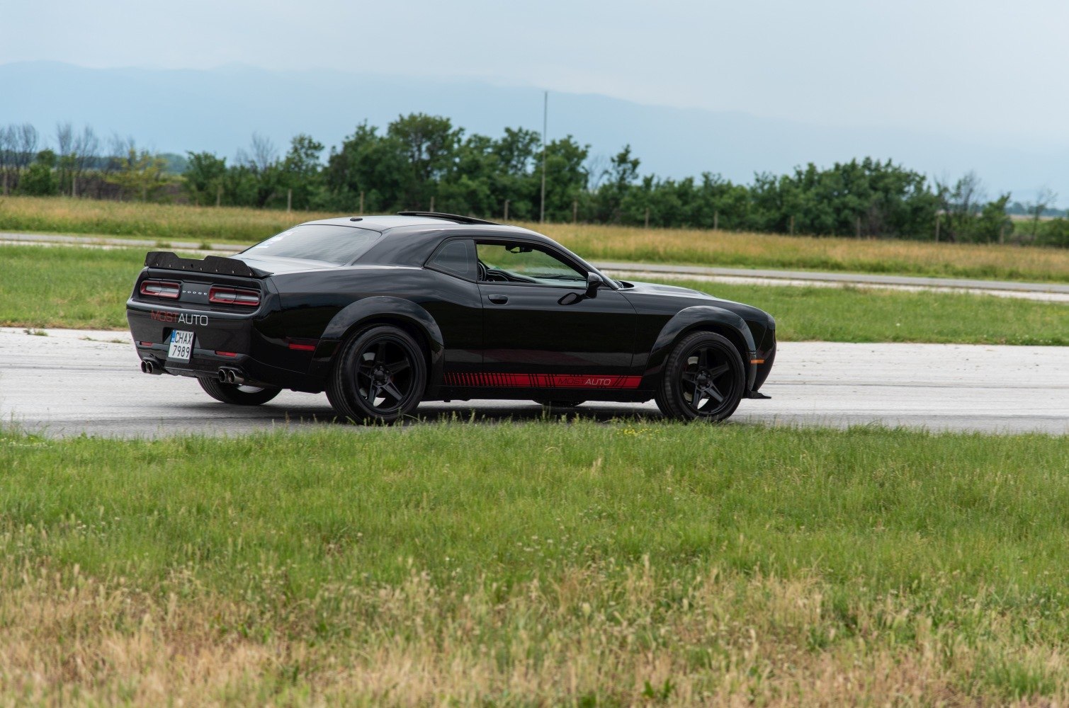 Black muscle coupe rear side view with wide tires and quad exhaust.
