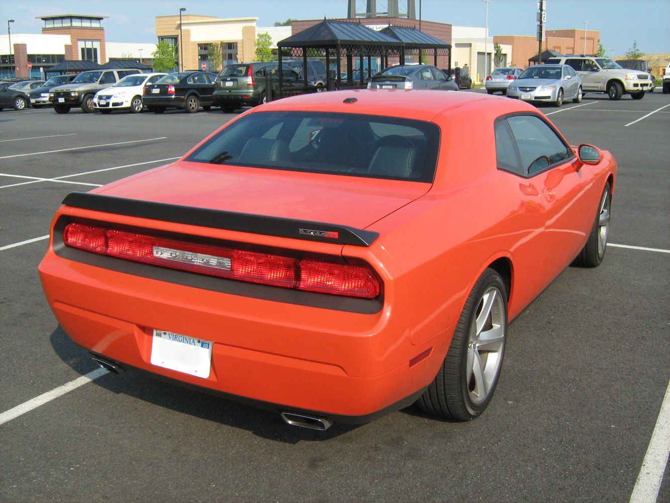 Rear view showing taillight, rear spoiler, and dual exhaust of a bright orange muscle car