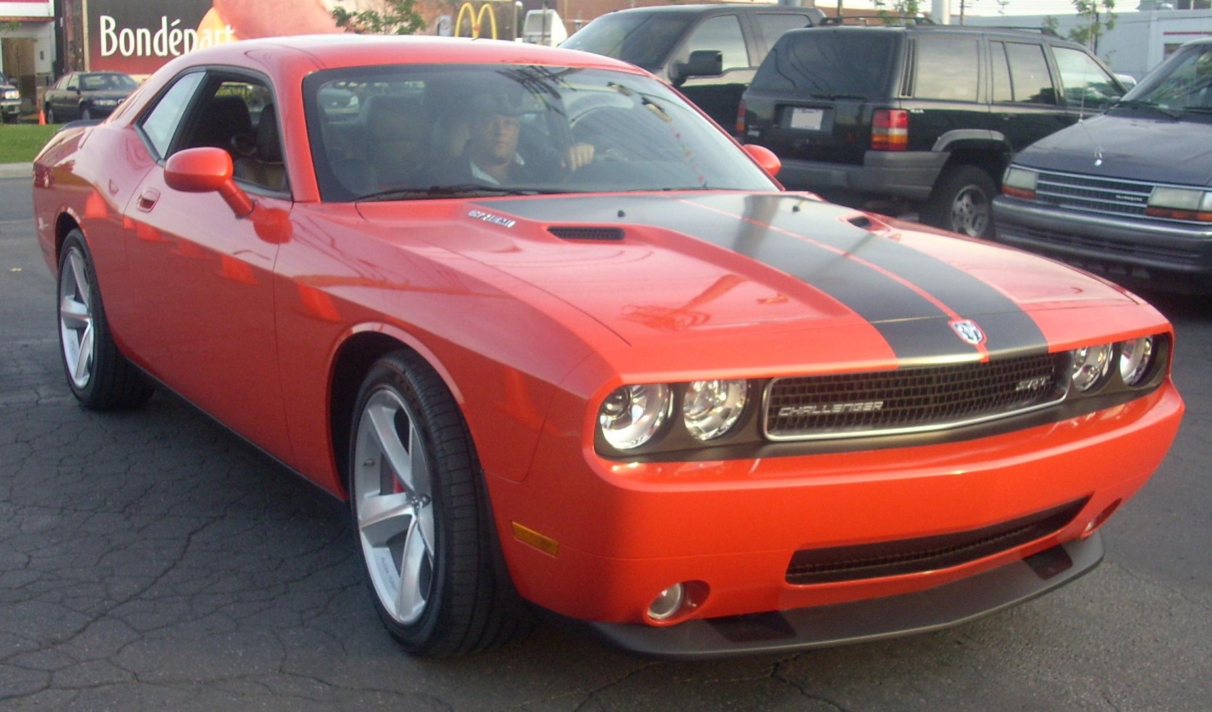 Front view of bright orange muscle car with racing stripe and aggressive grille
