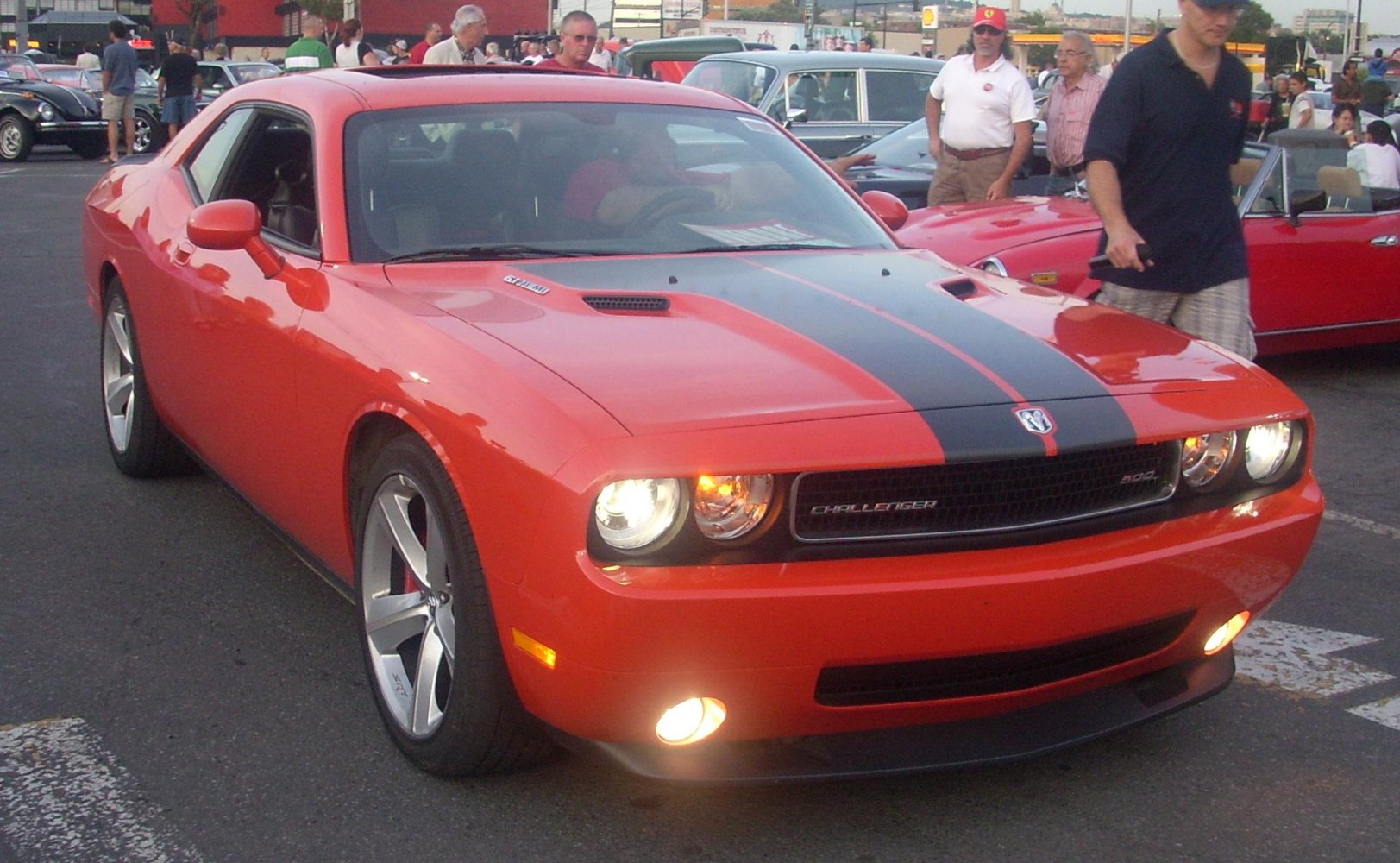 Front view of a red muscle car with black racing stripe and headlights on