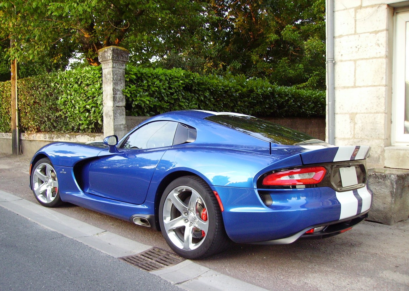Blue sports coupe rear side with white racing stripes and aerodynamic design