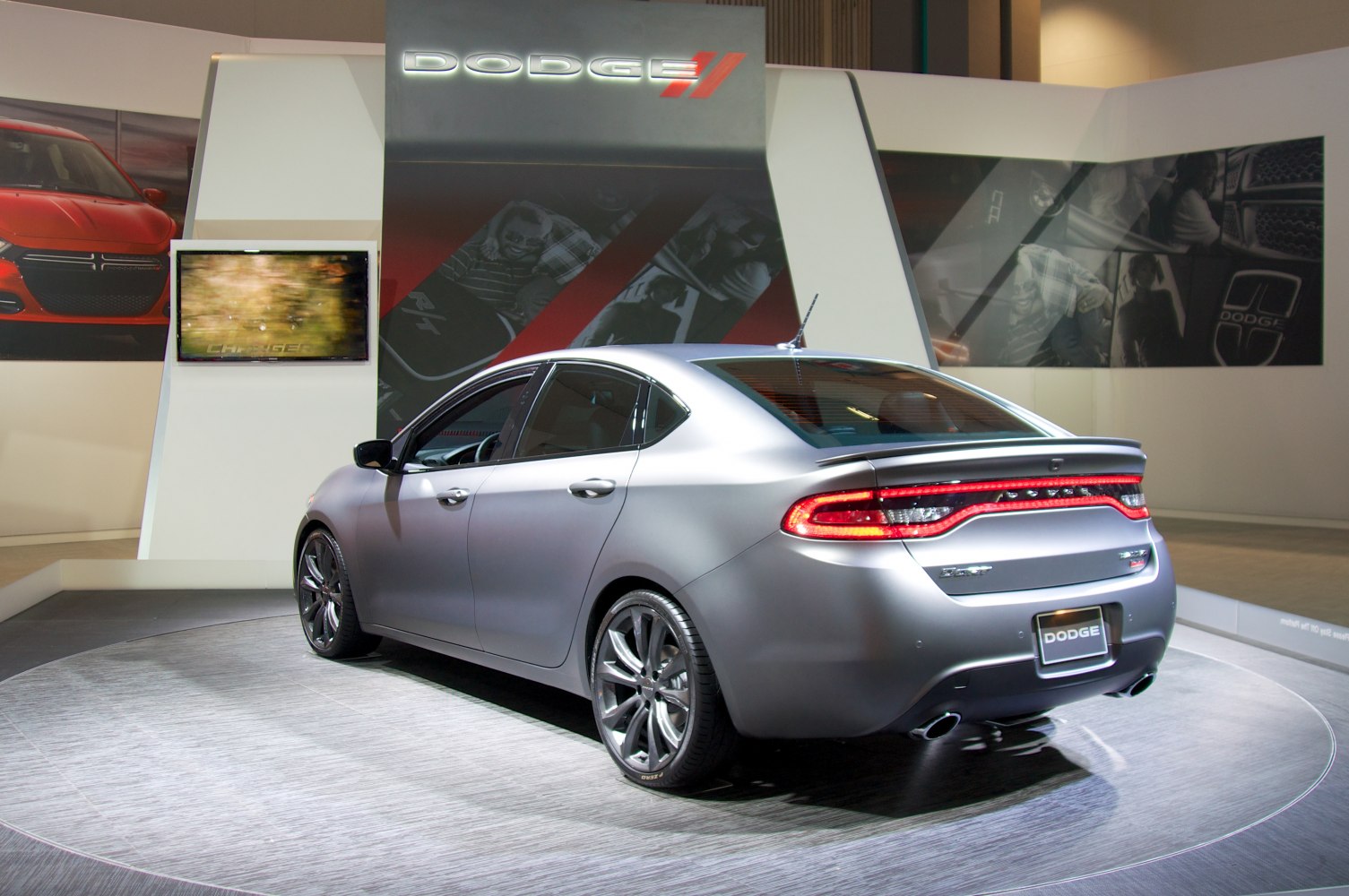 Rear three-quarter view of a sleek matte gray sedan with illuminated taillights and dual exhausts